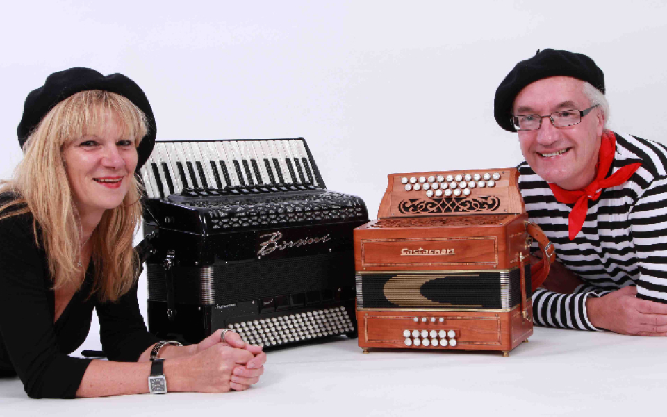 Kate Morris and Tony Croft dressed in French clothing lying next to an accordion and a melodeon against a white background